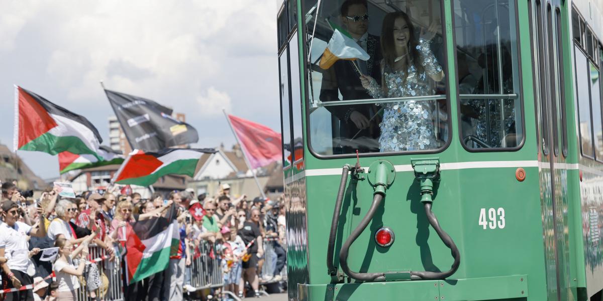 Az Írországot képviselő Emmy integet az Izrael-ellenes demonstrálóknak a 2025-ös Eurovízió nyitónapján Bázelben május 11-én 