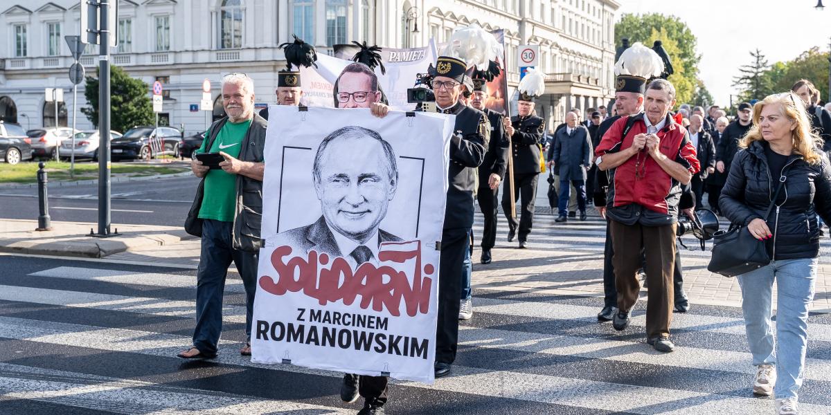 Egy demonstráló transzparenst tart a magasba Varsóban, rajta Vlagyimir Putyin orosz elnök képével és a „Szolidaritás Marcin Romanowskival” felirattal.