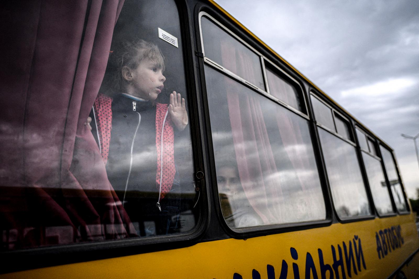 Egy lány néz ki egy buszból, miközben az orosz megszállás alatt álló zaporizzsjai területről származó családok érkeznek egy humanitárius konvojjal a belső menekültek regisztrációs és feldolgozó központjába Zaporizzsjában 2022. április 29-én, az Ukrajna el