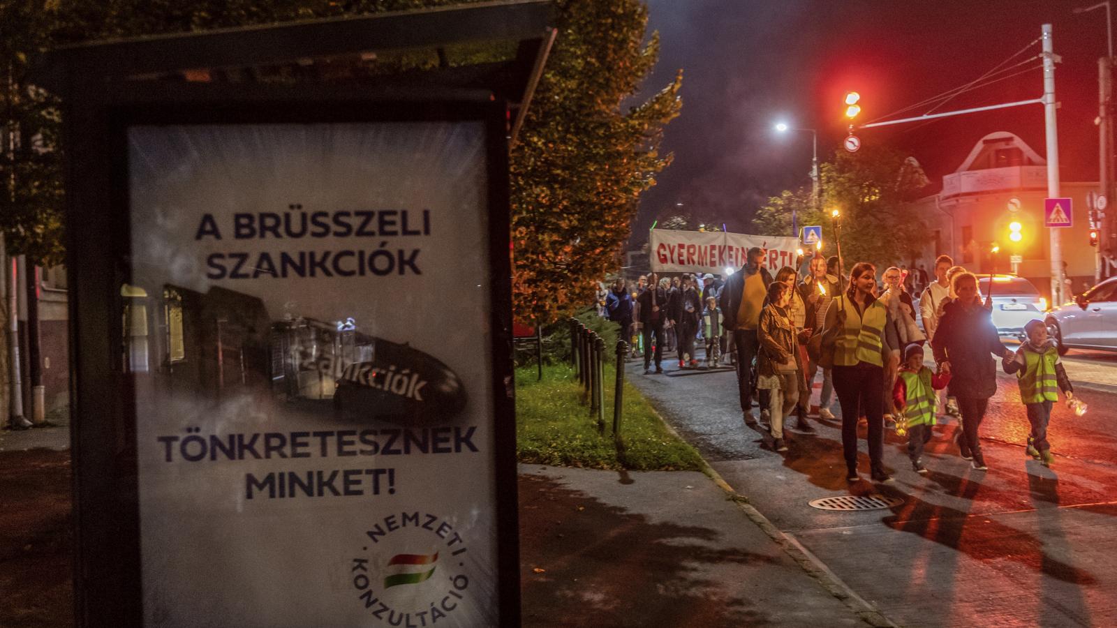 Kormányzati propagandaplakát előtt vonulnak a tanártüntetés résztvevői Budaörsön. A településeknek most azt a kormányzatot kellett volna segíteniük szignójukkal, amelyik nem ad elég pénzt tanáraik, iskoláik számára