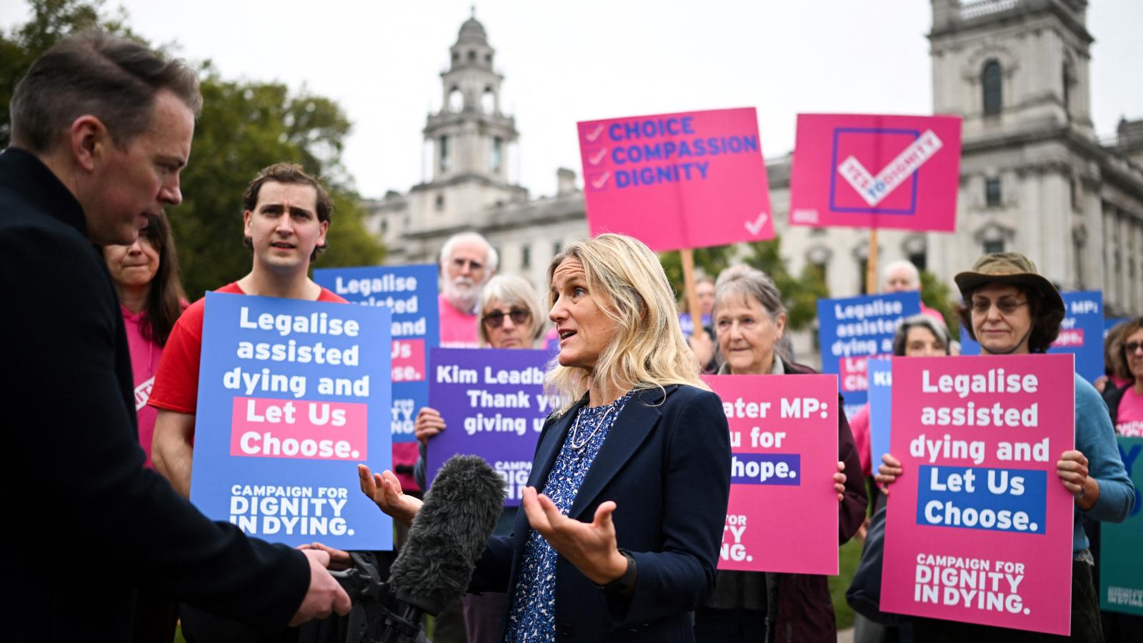 A törvényjavaslat szerdai benyújtásával egy időben a Méltósággal a Haldoklásban nevű szervezet demonstrációt tartott a Westminster-palota előtt az eutanázia legalizálása mellett (a képen Kim Leadbeater munkáspárti képviselő látható). A feliratokon ez áll: