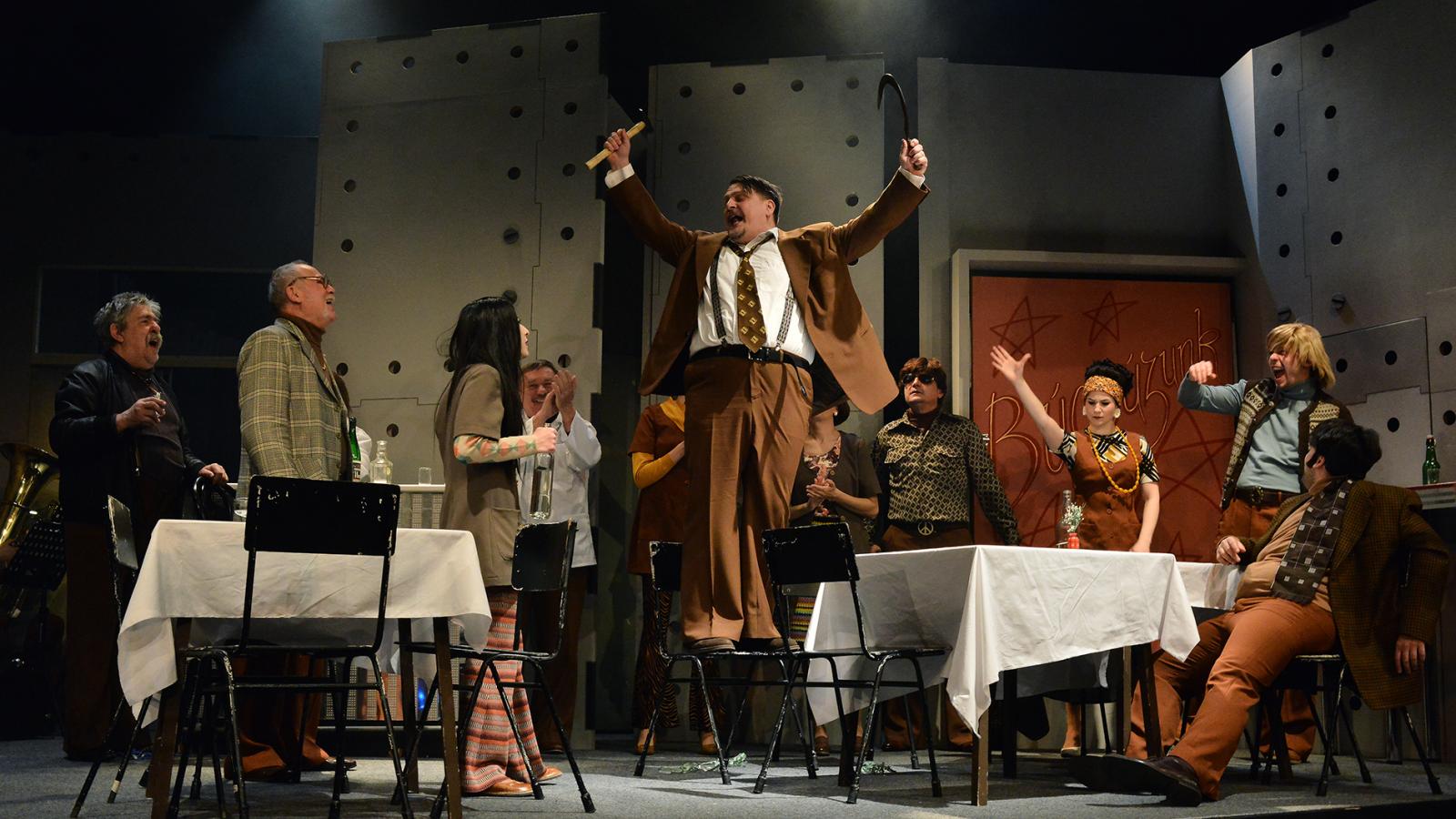 Az előadás fanyar kabaré jellegét erősítik a poénok, ám minden mondat mögött ott rejlik a groteszk helyzet szomorúsága is