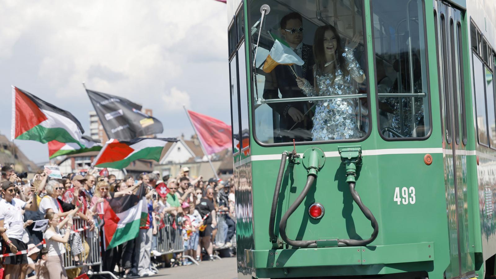 Az Írországot képviselő Emmy integet az Izrael-ellenes demonstrálóknak a 2025-ös Eurovízió nyitónapján Bázelben május 11-én 