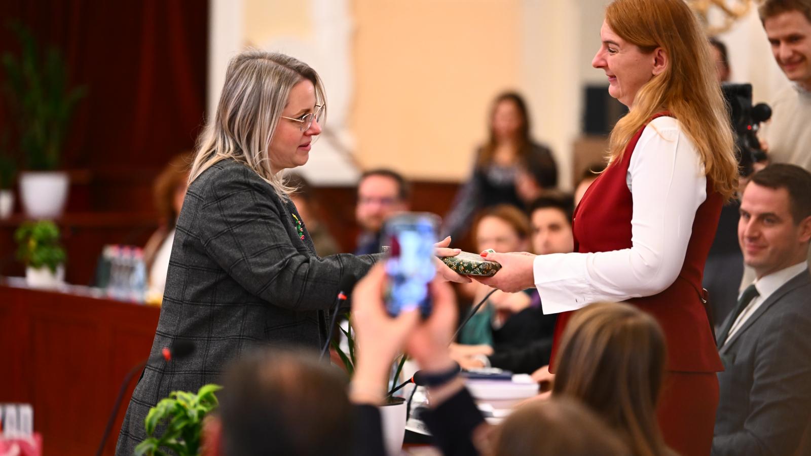 Szepesfalvy Anna adja át Baranyi Krisztina ajándékát, a Fővárosi Közgyűlésen, december 17-én