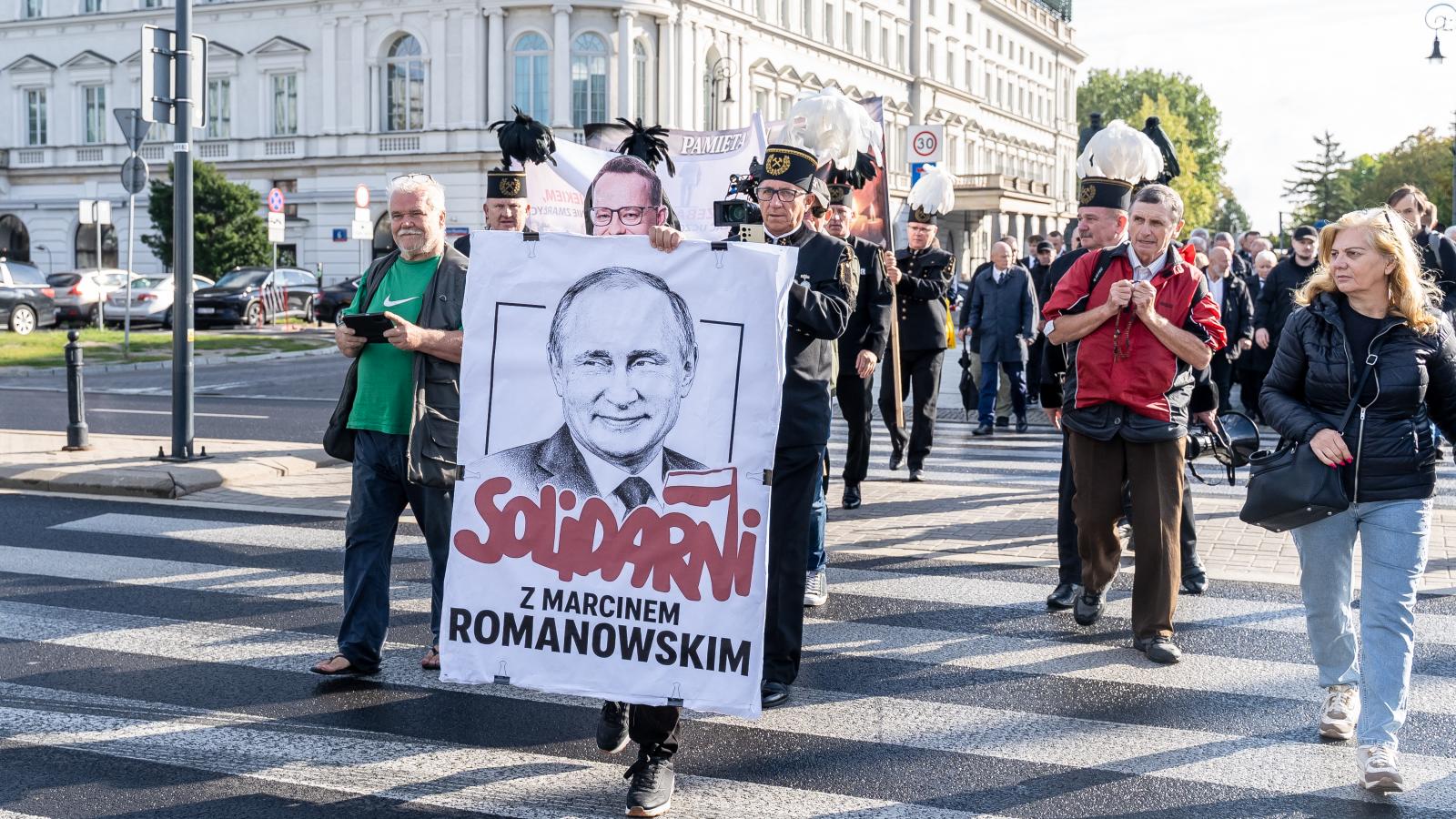 Egy demonstráló transzparenst tart a magasba Varsóban, rajta Vlagyimir Putyin orosz elnök képével és a „Szolidaritás Marcin Romanowskival” felirattal.