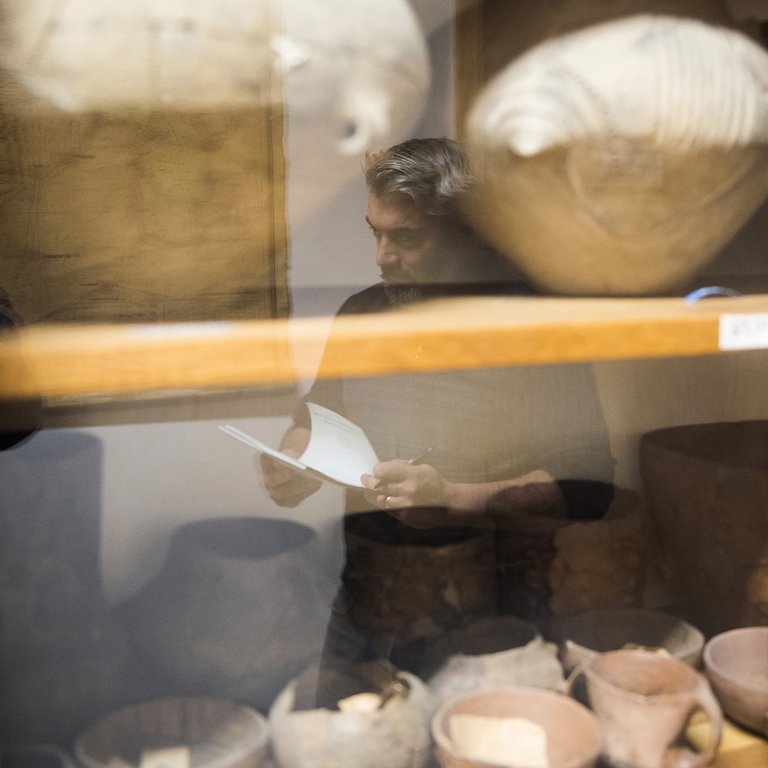 Pintye Gábor régész alakja tükröződik üvegezett szekrényben a múzeum régészeti részlegén