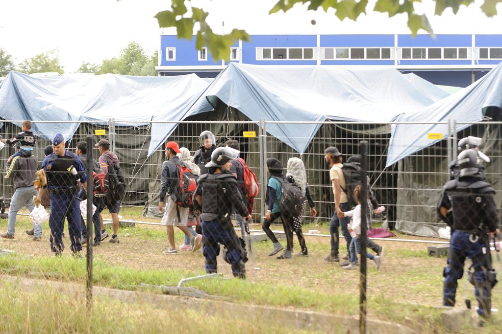 Családokat kísérnek ki a rendőrök a röszkei hangár kerítéssel körbevett részéről 2015. szeptember 4-én. Az idegenrendészeti előállítóhelyről két hullámban mintegy háromszáz illegális bevándorló tört ki. MTI Fotó: Kelemen Zoltán Gerge