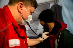 A Magyar Vöröskereszt egészségügyi gyorsbeavatkozó egységének tagja vizsgál egy menekültet &nbsp;a görög-macedón határ görög oldalánMTI Fotó: Balogh Zoltá